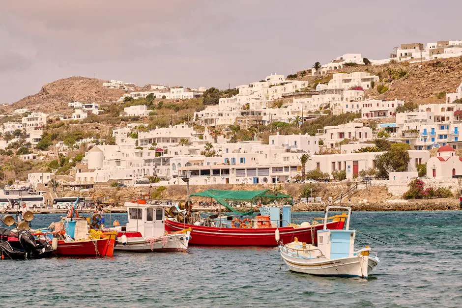 Charming white buildings and vibrant boats in Mykonos harbor on a sunny summer day.