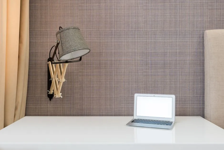 Interior of workplace with opened netbook on white table near wall with lamp